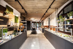 Una moderna disposición tipo buffet con varias estaciones de comida, techo de madera y plantas en macetas.