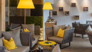 A modern lounge area with grey upholstered sofas and armchairs, yellow cushions, and a coffee table with drinks. - Die Wasnerin G'sund & Natur Hotel (Bad Aussee)