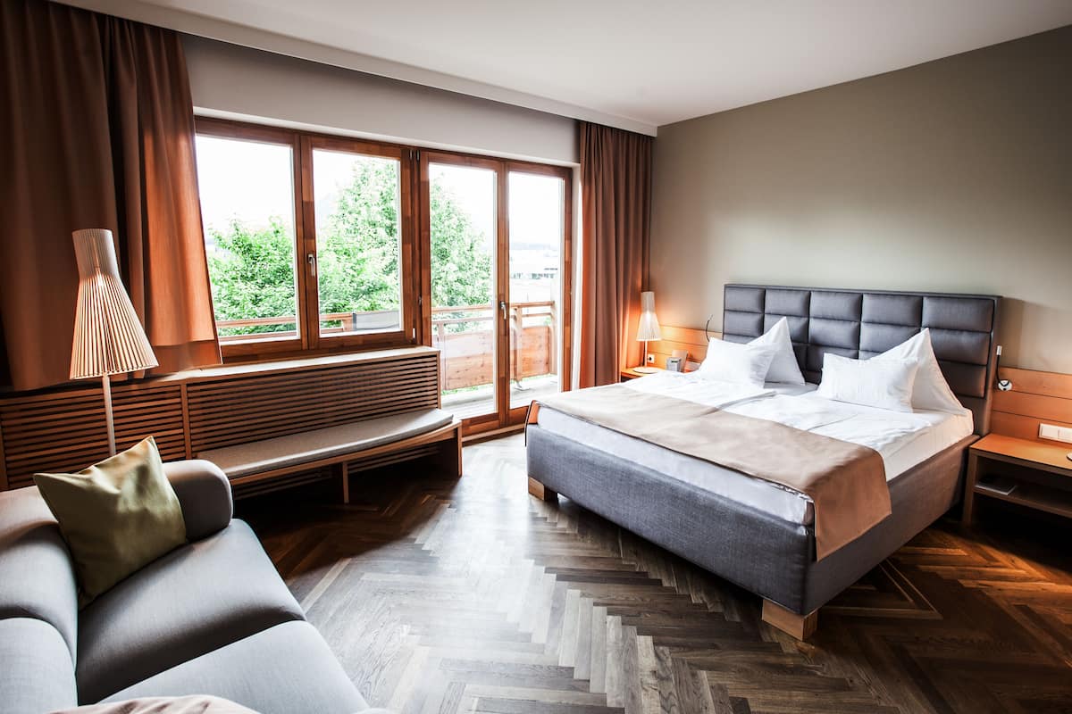 Una habitación de hotel moderna con una cama grande, un sofá, un banco y vistas a zonas verdes.