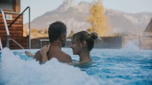 A couple in a hot tub with a mountain view in the background. - Die Wasnerin G'sund & Natur Hotel (Bad Aussee)