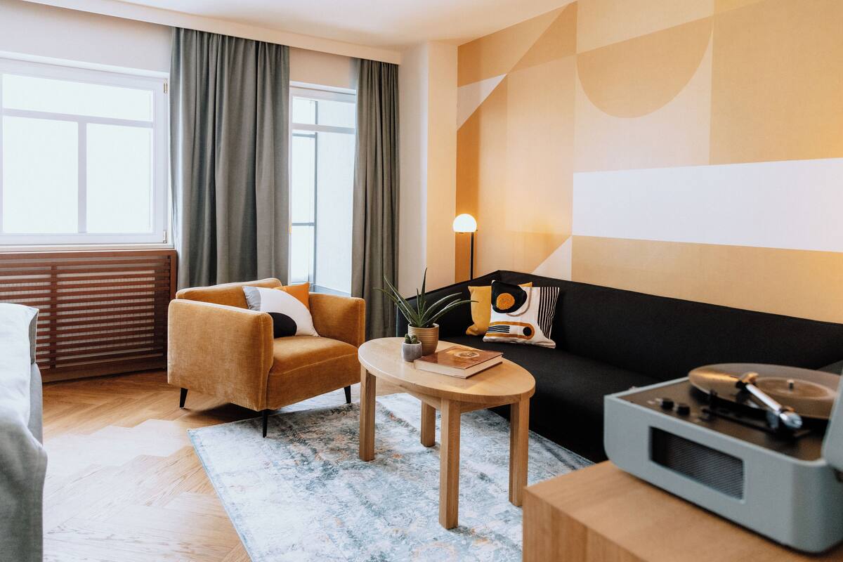Una habitación de hotel moderna con sofá, sillón, una mesita y un tocadiscos.