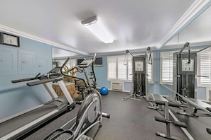 A gym with exercise equipment, a clock, and a window with blinds.