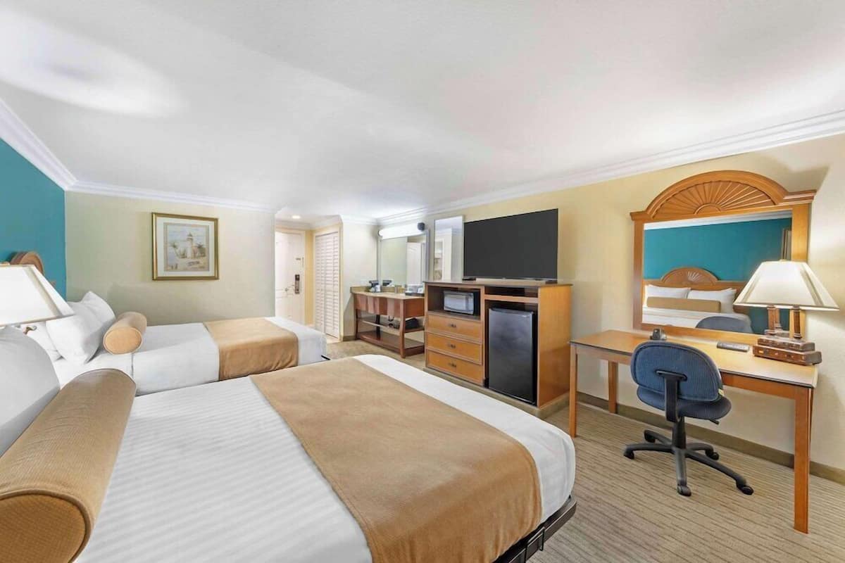 A hotel room with two beds, a desk, a television, and a mirror.