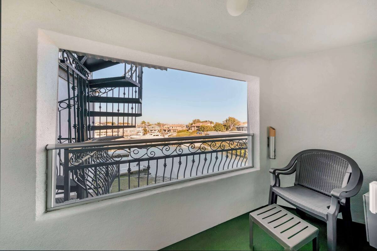 A balcony with a view of buildings and trees, a metal railing, a bench, and a small table.