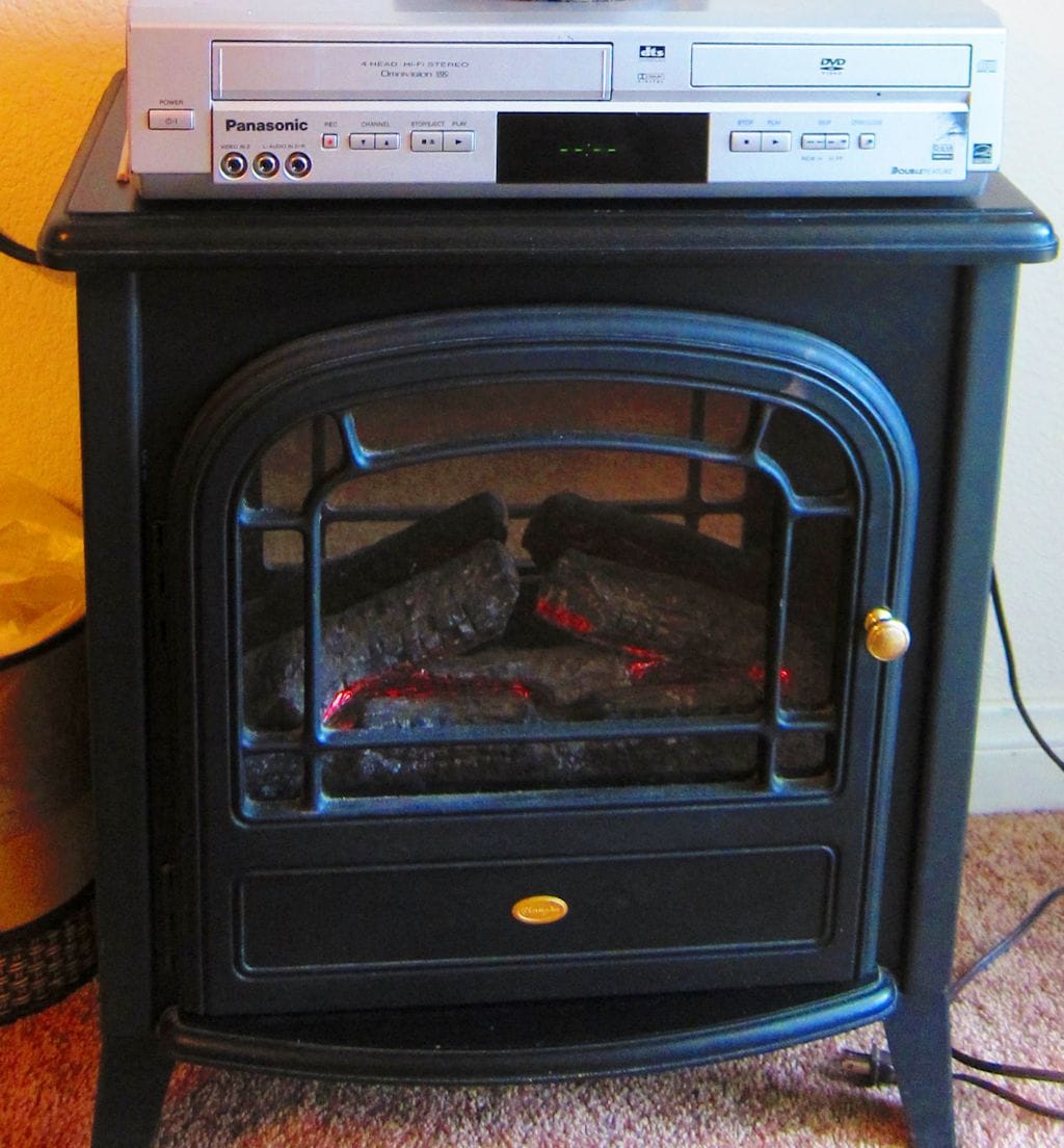A black wood-burning stove with a digital control panel and a Panasonic DVD player on top.