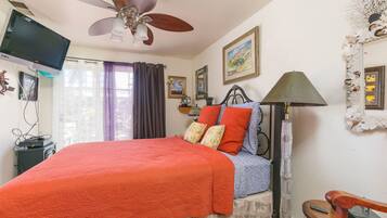 A bedroom with a bed, a ceiling fan, a television, and a lamp.