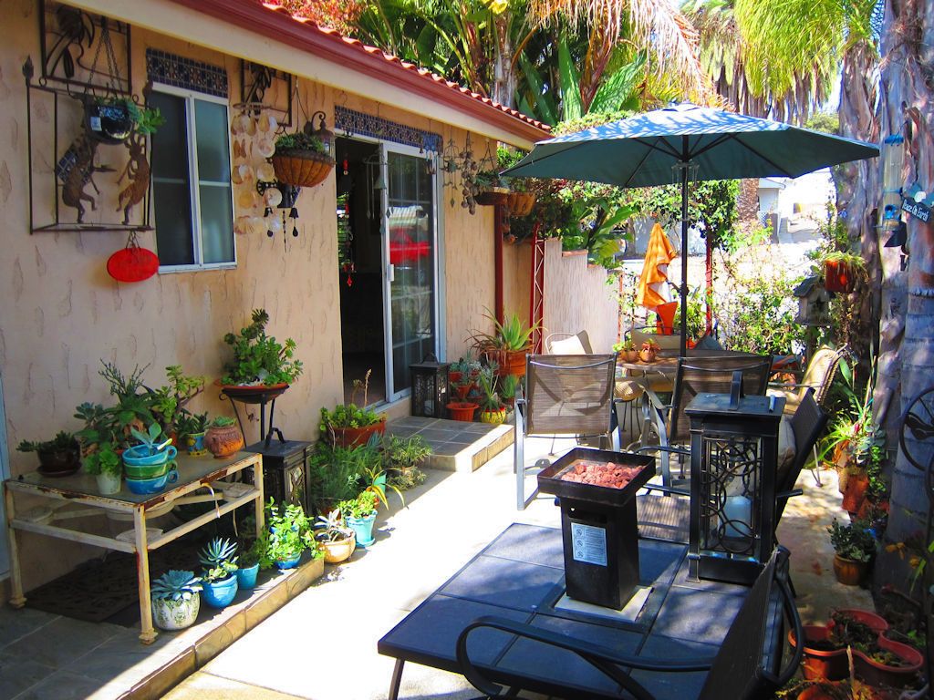 An outdoor patio with a table and chairs, surrounded by potted plants and a variety of hanging decorations.