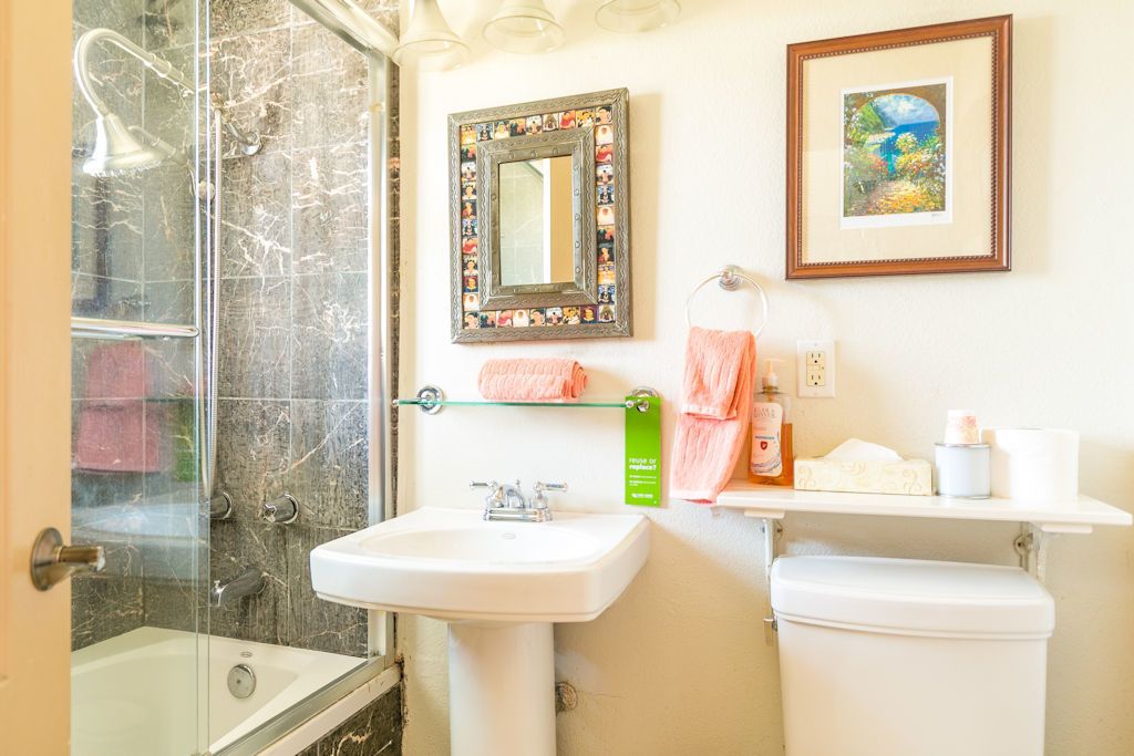 Ein Badezimmer mit Duschkabine aus Glas, Waschbecken in Weiß, Toilette, Spiegel mit Rahmen und Ablage für Toilettenartikel.