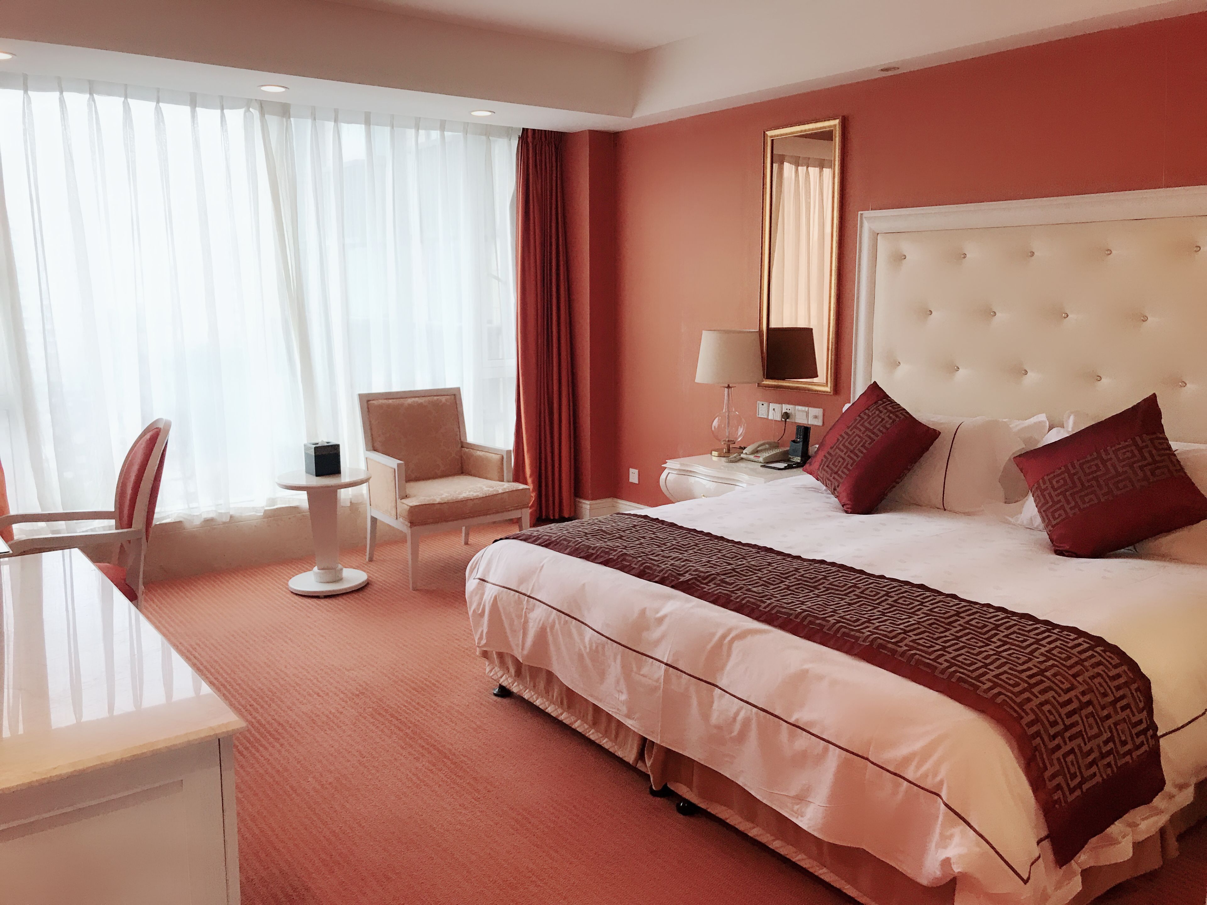 Een hotelkamer met een groot bed, een bureau, een stoel, een nachtkastje en een spiegel.
