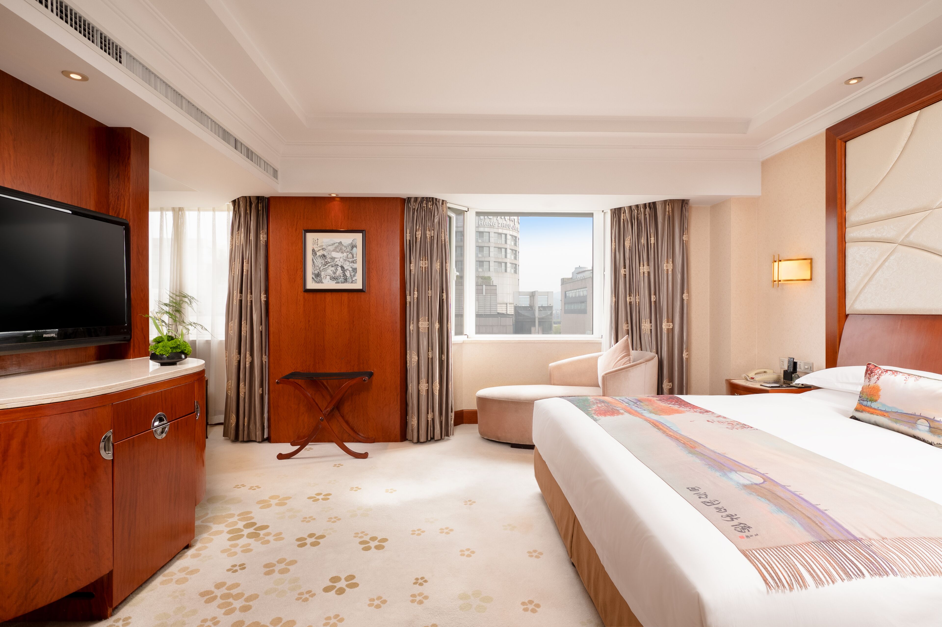 Hotelkamer met een groot bed, een flatscreen televisie, een houten dressoir, een stoel, een klein tafeltje en een raam met uitzicht op de stad.