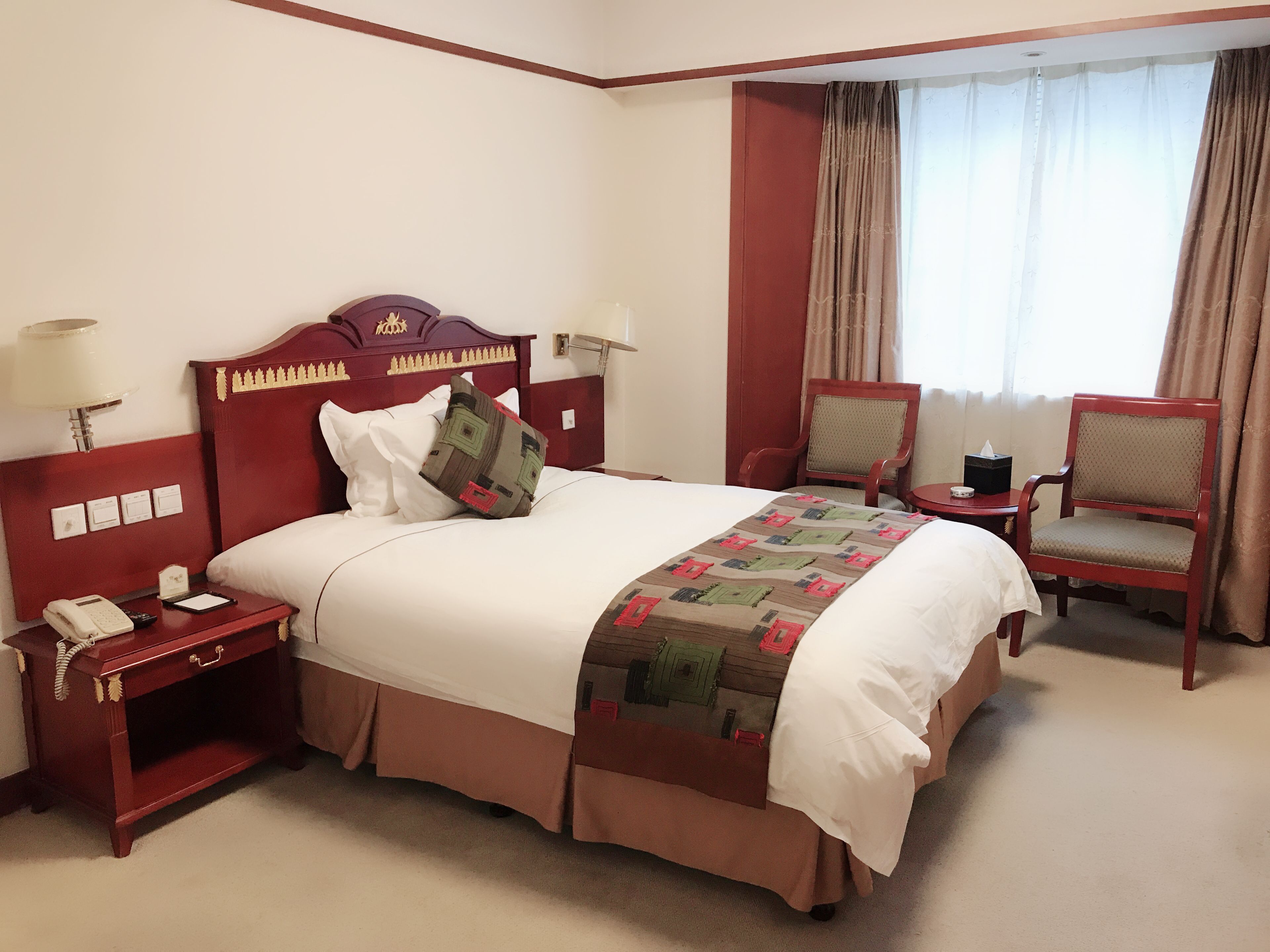 A hotel room with a large bed, two chairs, a nightstand with a phone, and a bedside table.