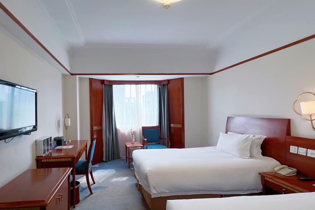 A hotel room with a bed, a desk, a chair, a TV, and a window with curtains.