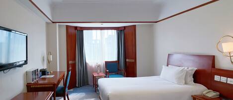 Une chambre d’hôtel avec un lit, un bureau, une chaise, une télévision et une fenêtre avec des rideaux.