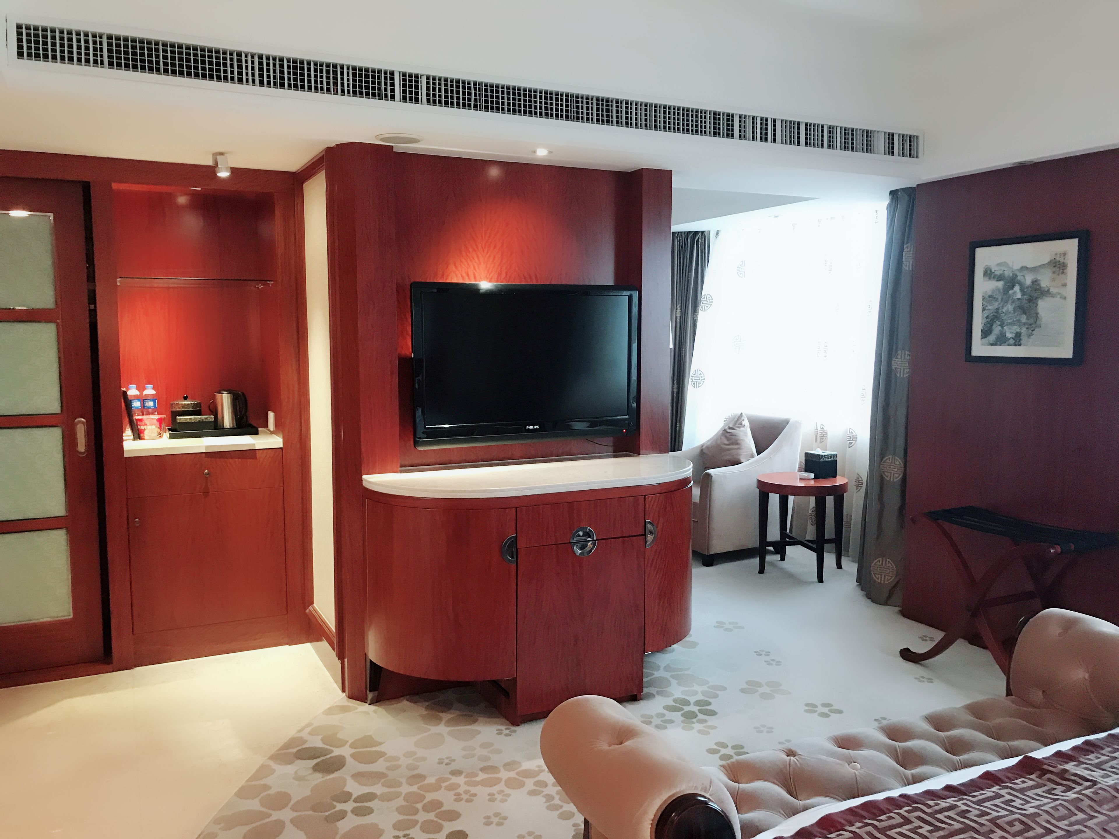 Ein Hotelzimmer mit einem großen Flachbildfernseher an einem Holzkasten, einer Couch, einem kleinen runden Tisch und einem Bett mit einem gemusterten Überwurf.