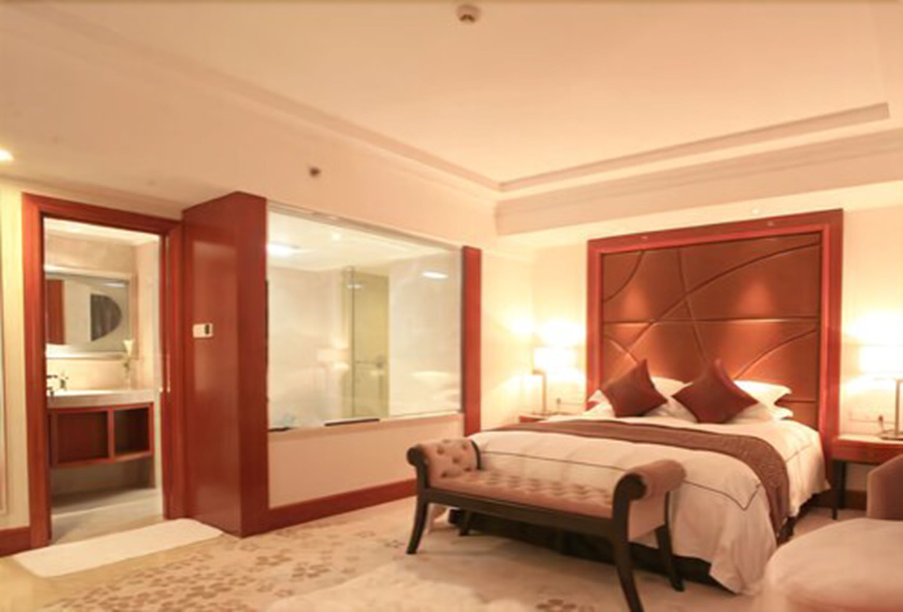 Habitación de hotel con una cama grande, una mesita de noche, un espejo y un baño visible a través de una puerta abierta.