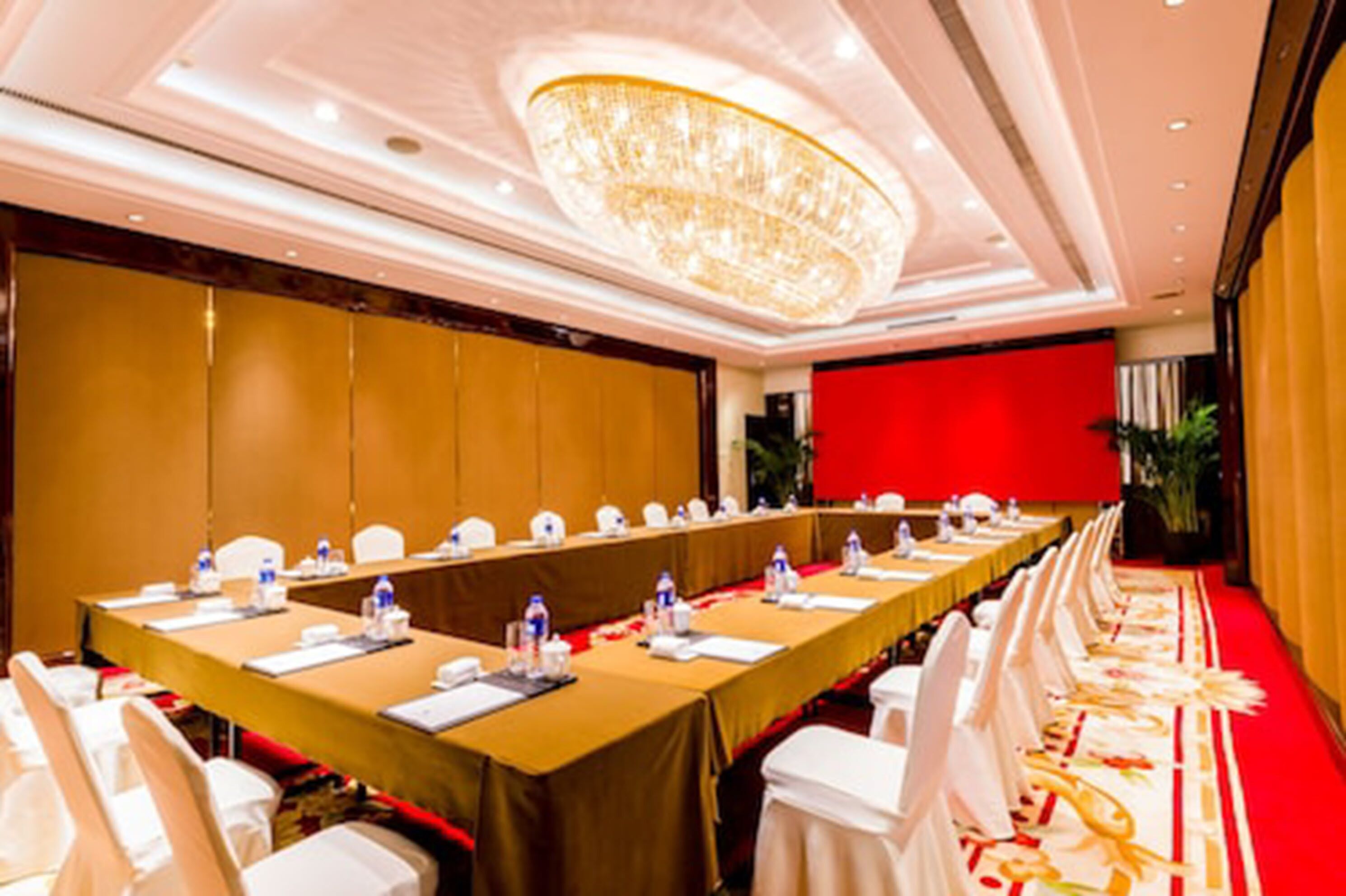 A conference room with a long table, white chairs, and a red accent wall.