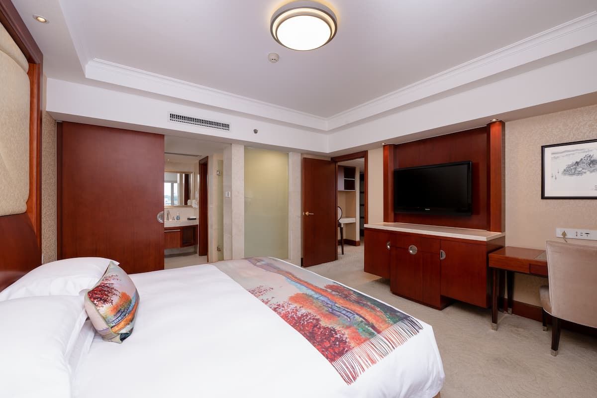 A hotel room with a bed, a TV, a desk, and a bathroom visible through an open door.