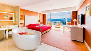 Habitación de hotel con una cama grande, una bañera con pétalos de rosa, un escritorio, un televisor y vistas a las montañas.