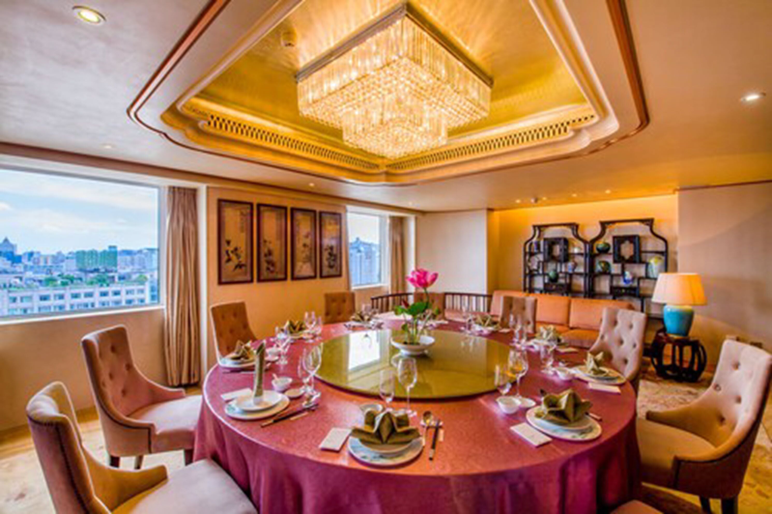 A dining room with a round table set for six, surrounded by upholstered chairs.