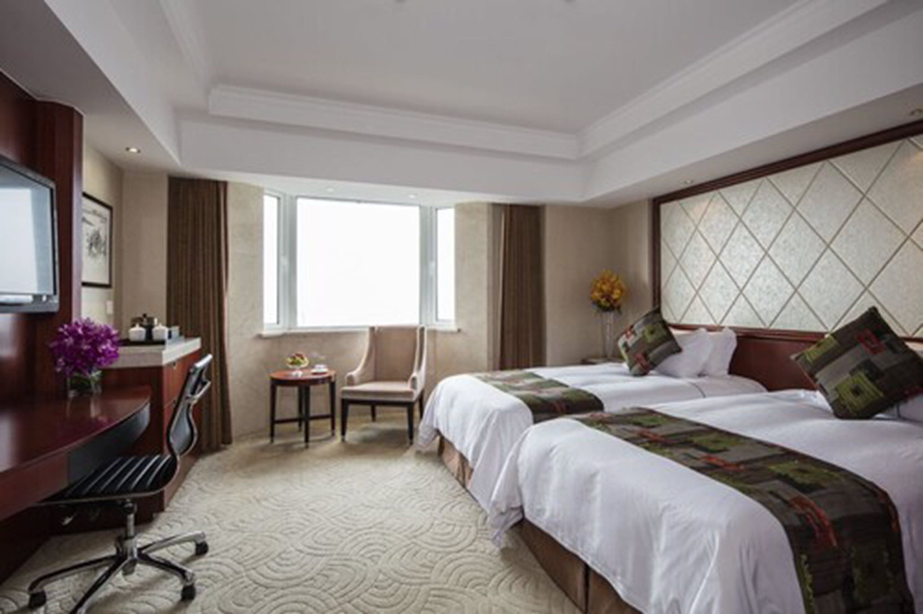 A hotel room with two beds, a desk with a chair, a small table, and a window.