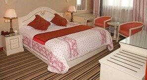A hotel room with a bed, bedside tables, a desk, a chair, and a small table.
