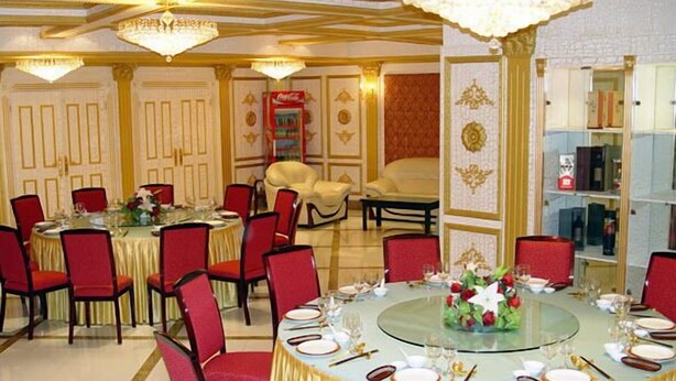 A formal dining room with round tables, red chairs, and gold accents.