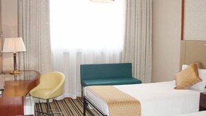 A hotel room with a bed, a chair, a desk, a lamp, and a window with curtains.