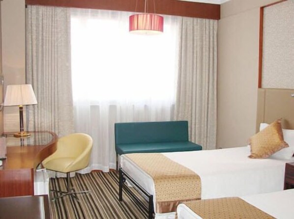 A hotel room with a bed, a chair, a desk, a lamp, and a window with curtains.