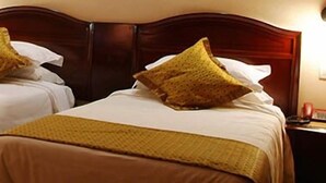 A hotel room with two beds, each with a brown blanket and pillows, a wooden headboard, and a dark-colored sofa in the corner.