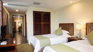 A hotel room with two beds, a desk, a wardrobe, and a bathroom visible in the background.