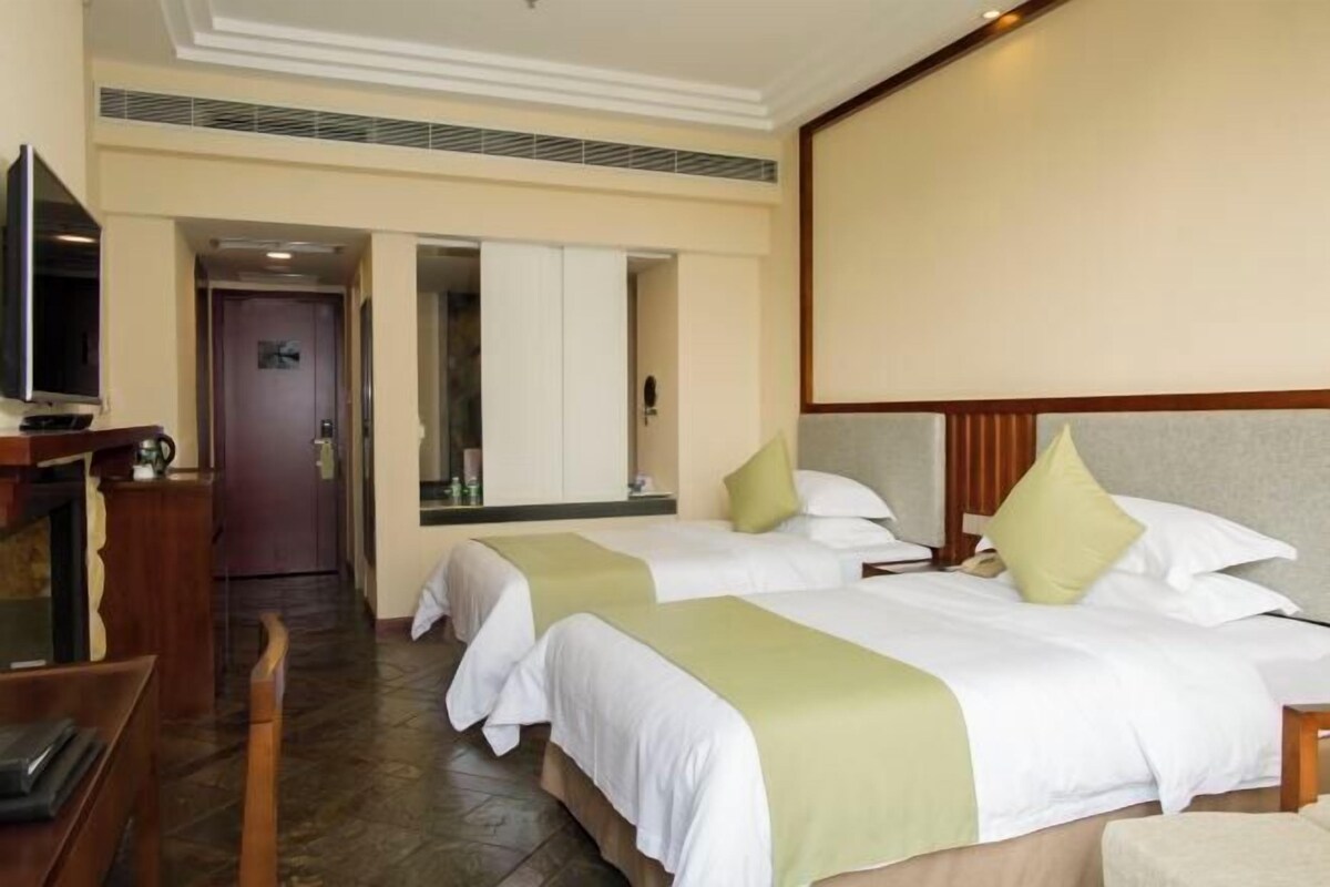 A hotel room with two beds, a television, a desk, and a mirror.