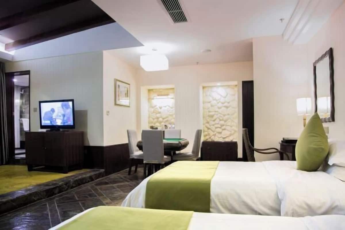 Habitación de hotel con dos camas, televisión, zona de comedor y baño.