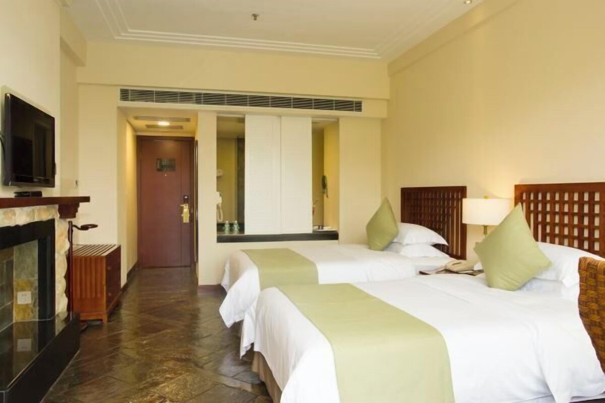 A hotel room with two beds, a television, a fireplace, and a mirror.