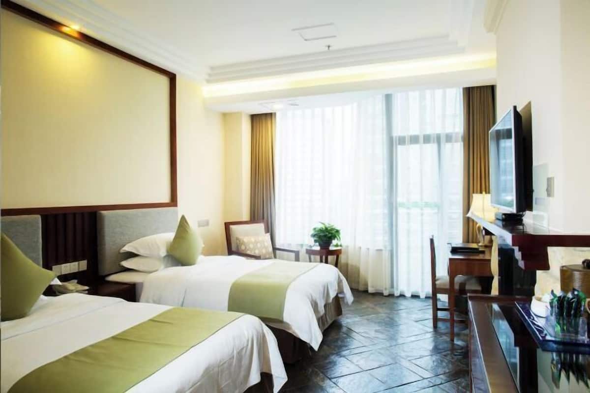 Habitación de hotel con dos camas, televisión, escritorio y ventana con cortinas.