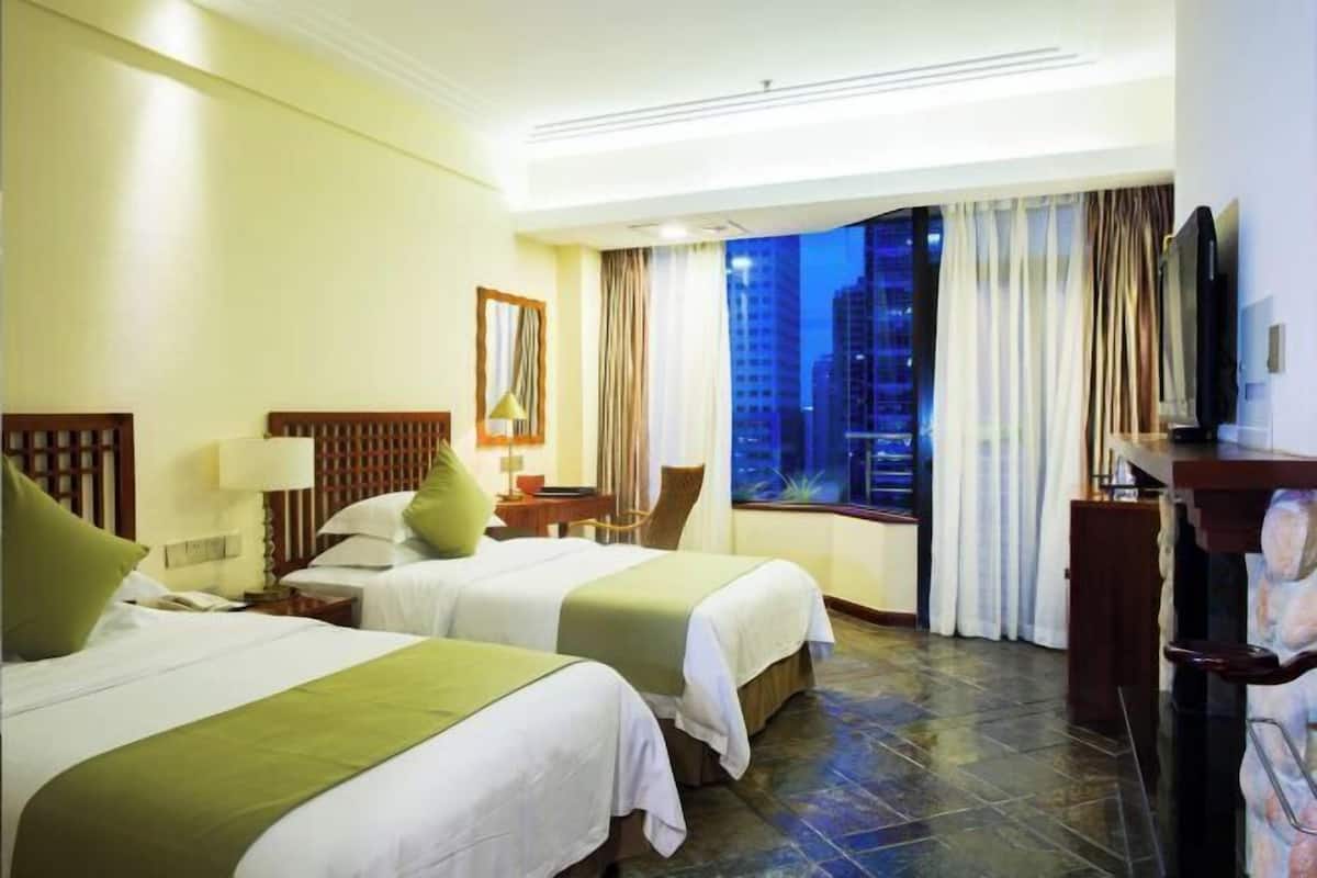 Habitación de hotel con dos camas, un escritorio, una silla, un televisor y una ventana con vista a la ciudad.