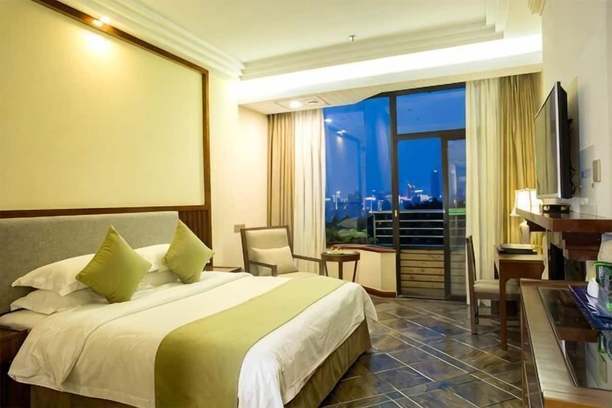 Habitación de hotel con una cama grande, un escritorio, una silla, un televisor y vistas a la ciudad de noche.