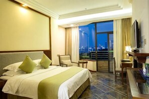 A hotel room with a large bed, a desk, a chair, a TV, and a view of the city at night. - 88 Eling Park Hotel (Chongqing Eling Erchang) (Chongqing)