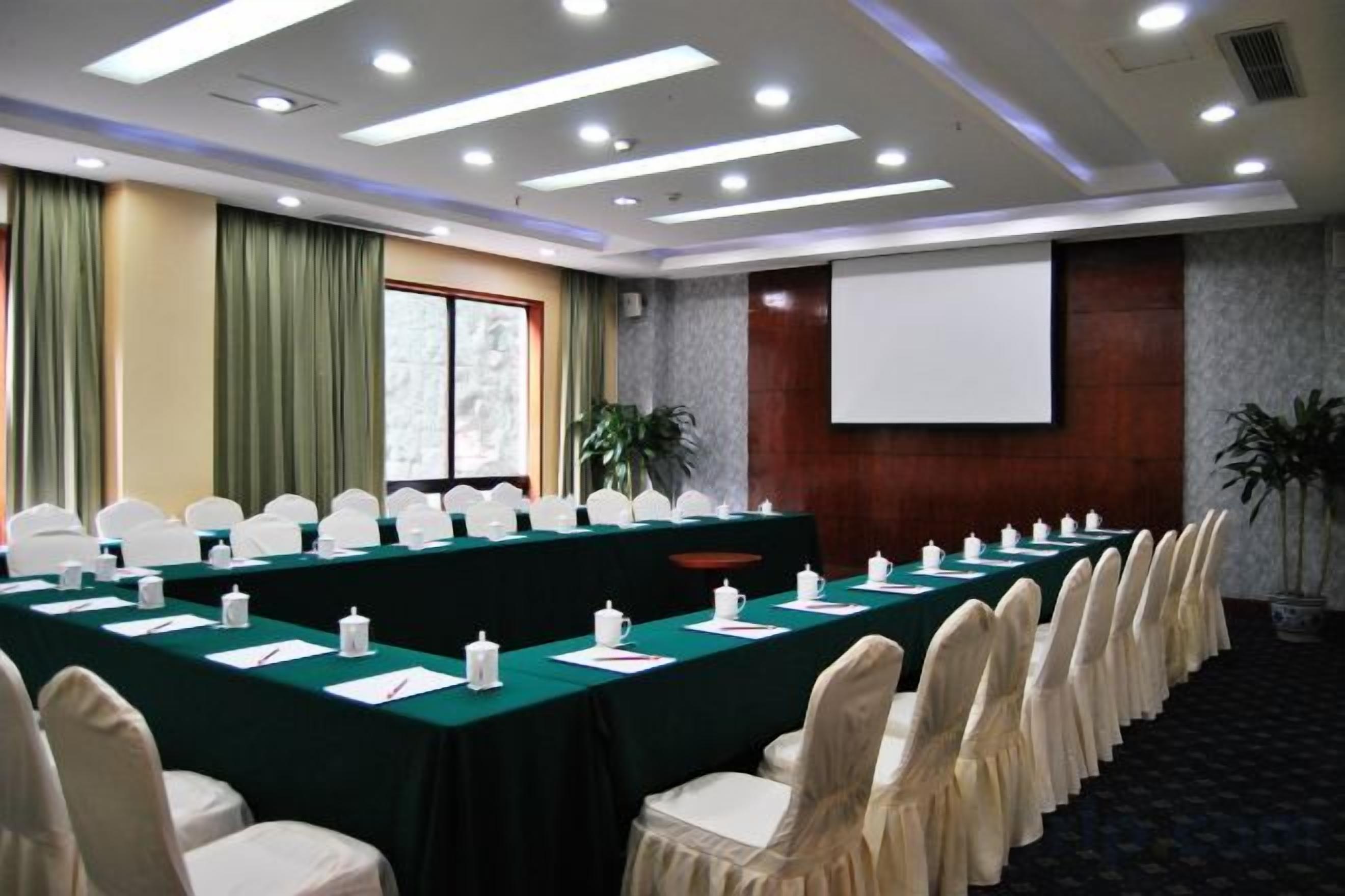 A conference room with a long table, chairs, a projector screen, and a plant.