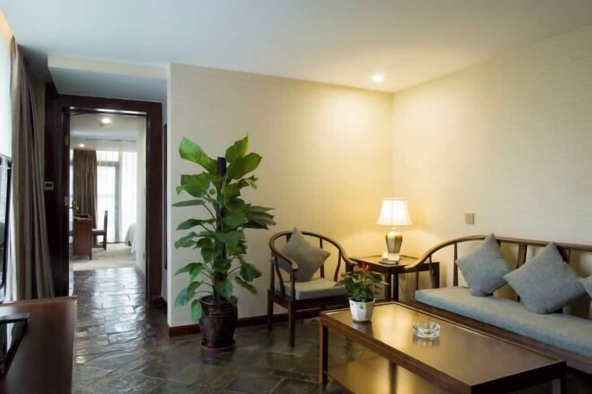 Una habitación de hotel con sofá, sillas, una mesa de centro, lámpara y planta en maceta.