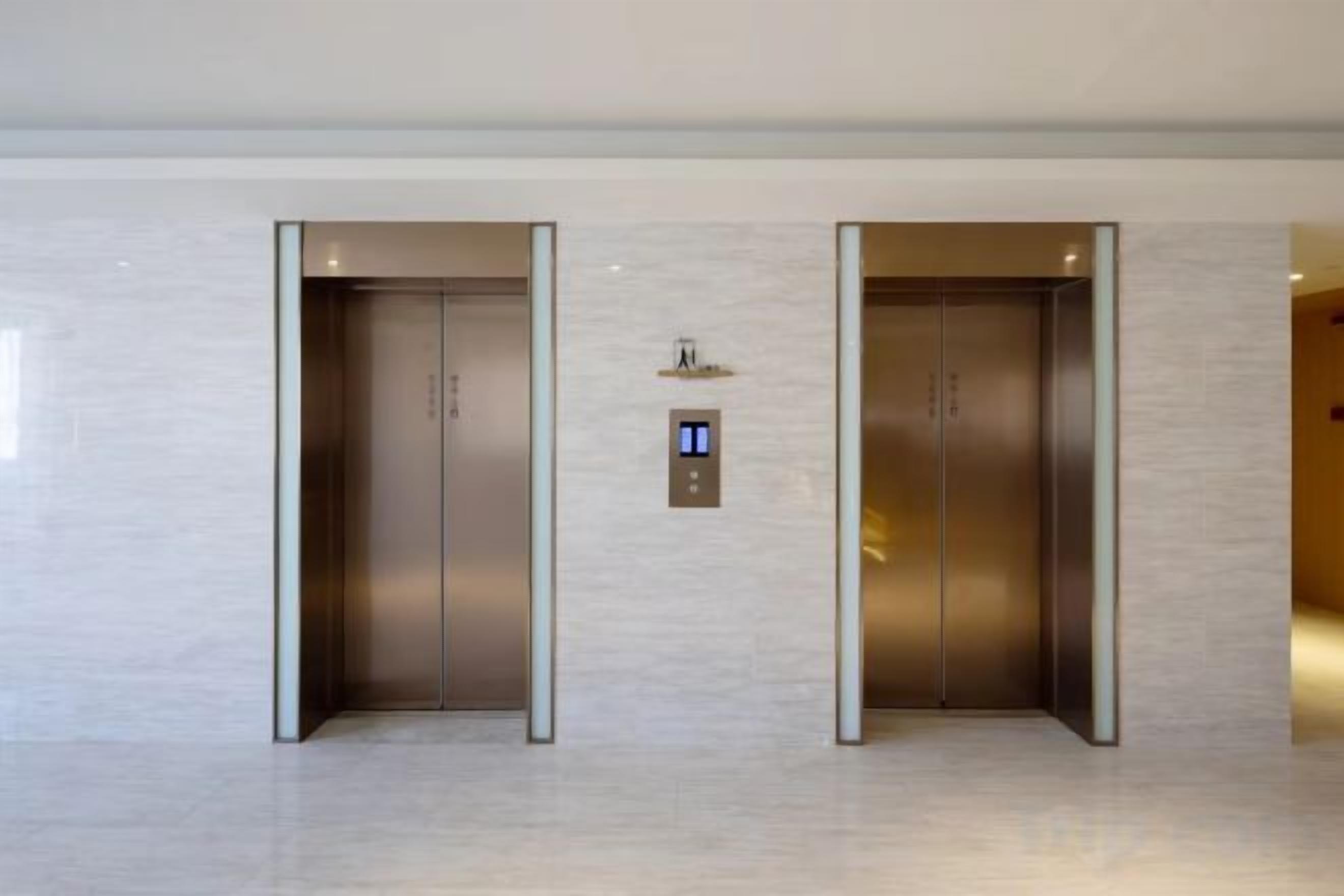 Two elevator doors with a digital display above them, set in a modern building interior.