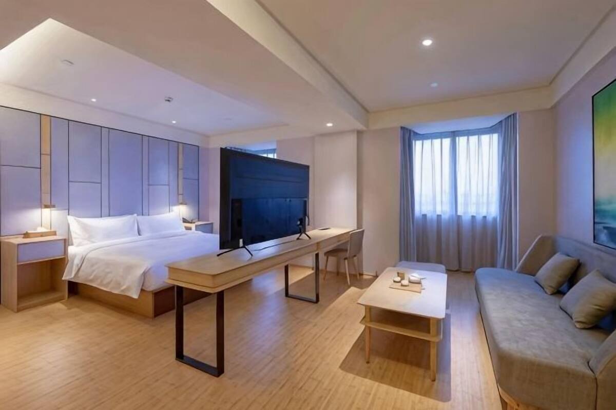 A modern hotel room with a bed, a desk, a sofa, and a TV.