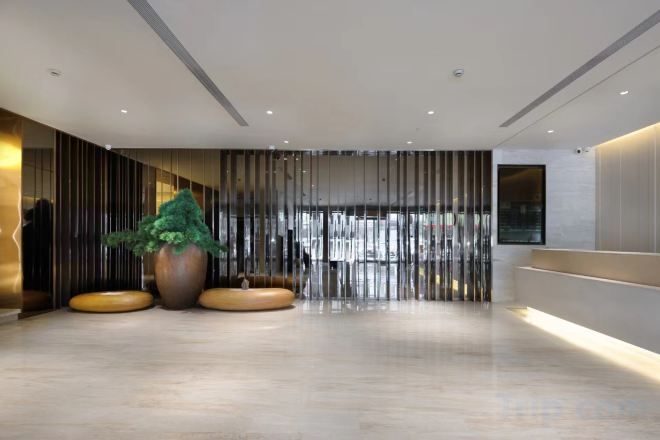 A modern lobby with a reception desk, seating area, and a large potted plant.
