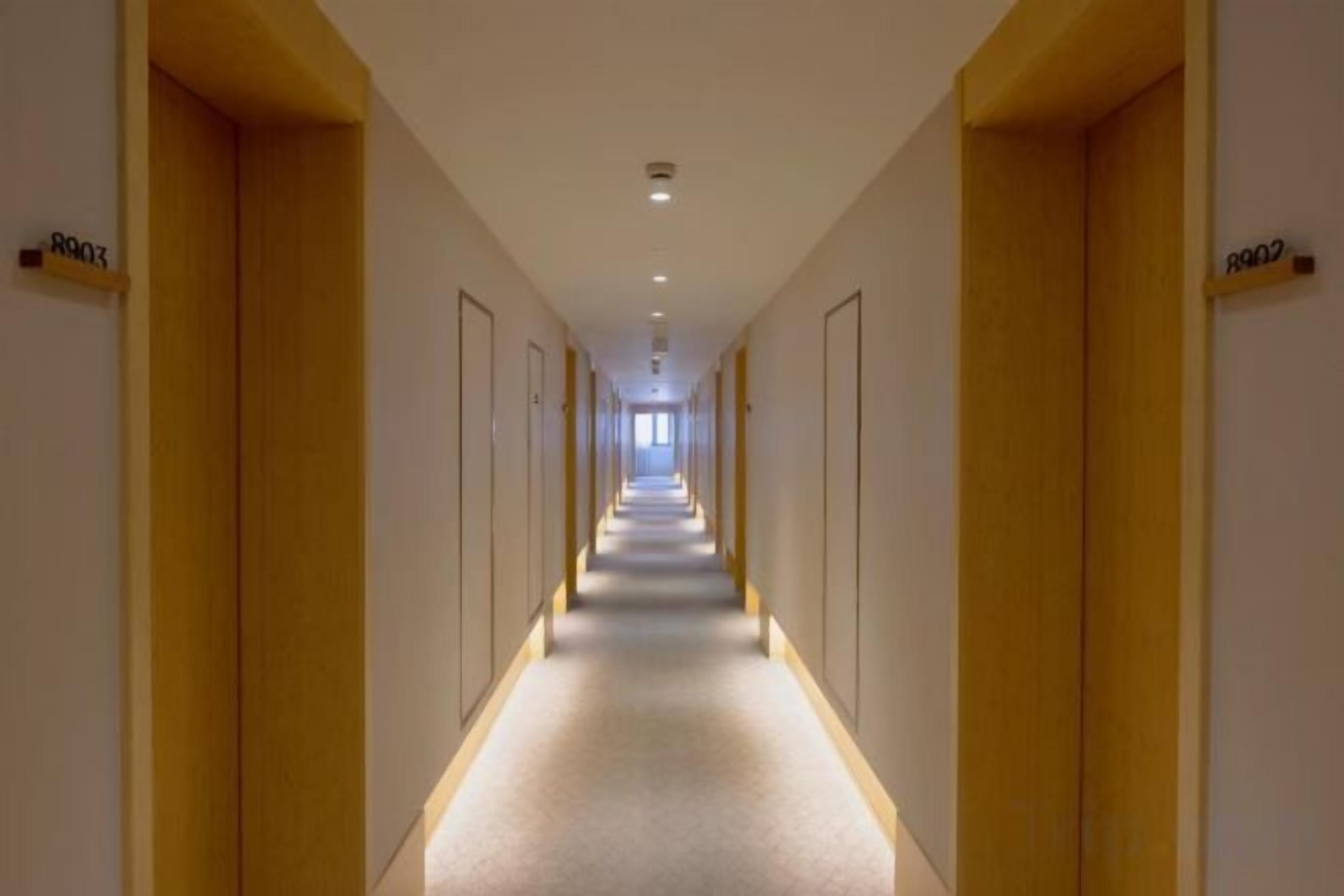 Een hotelgang met deuren voorzien van kamernummers, een vloerbedekking en een plafondlamp.