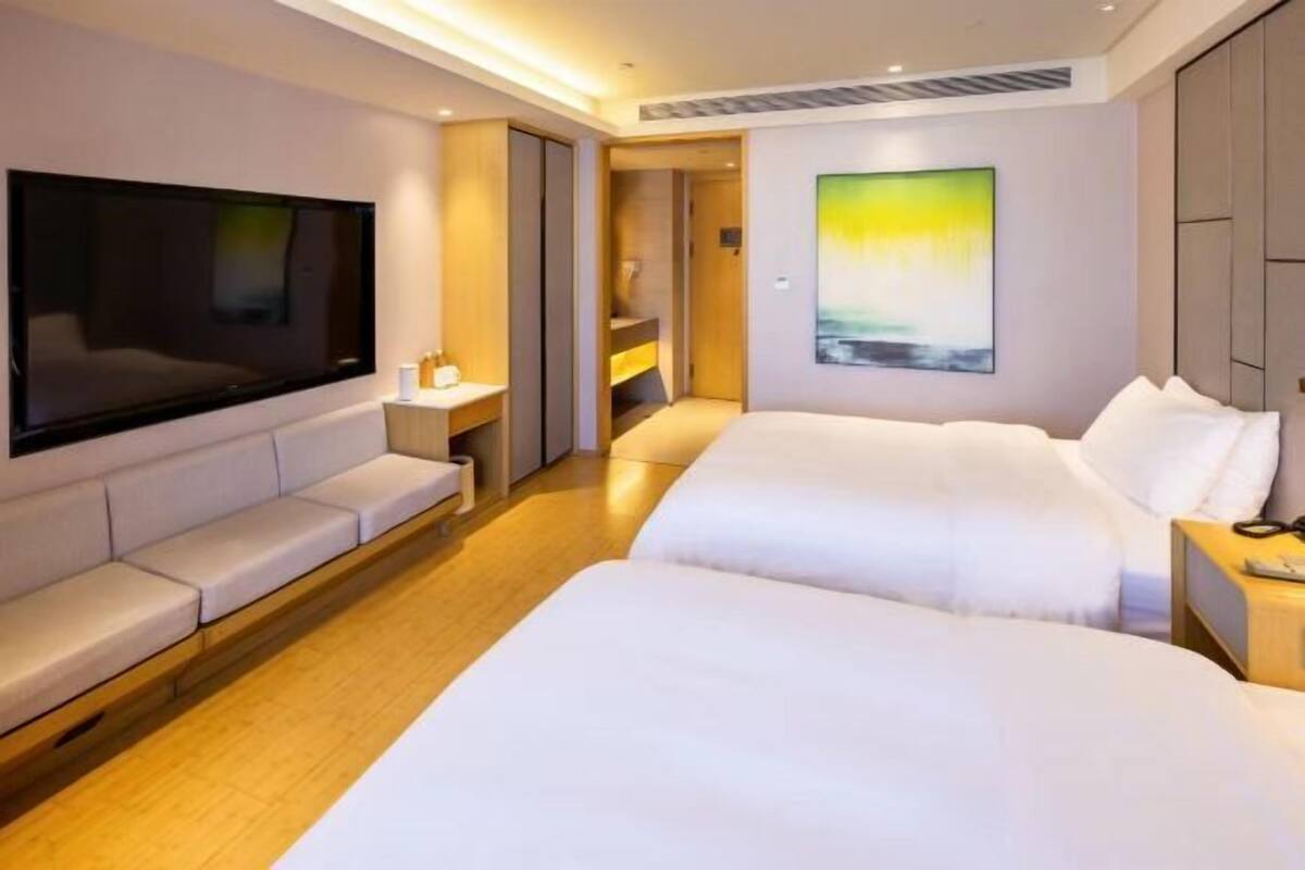 A modern hotel room with a large flat-screen TV, a sofa, two beds, and a painting on the wall.