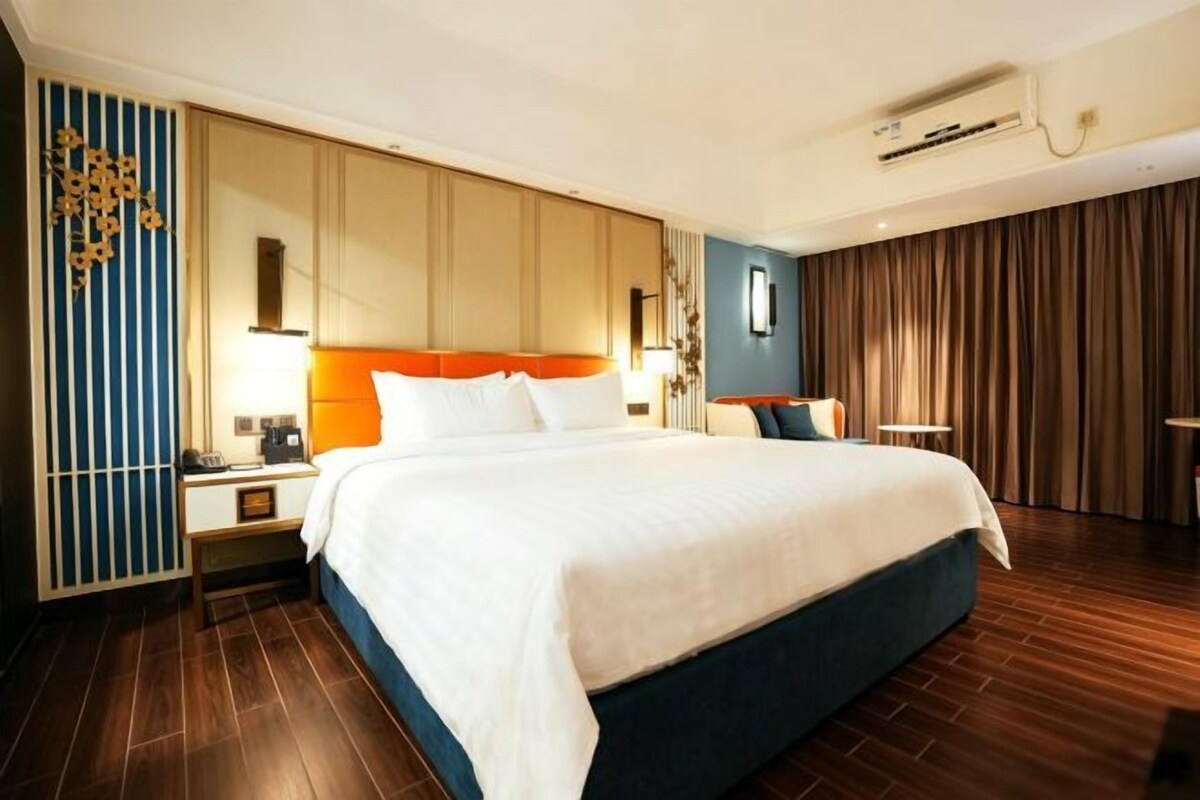 A hotel room with a large bed, a nightstand, a lamp, and a wall-mounted air conditioner.