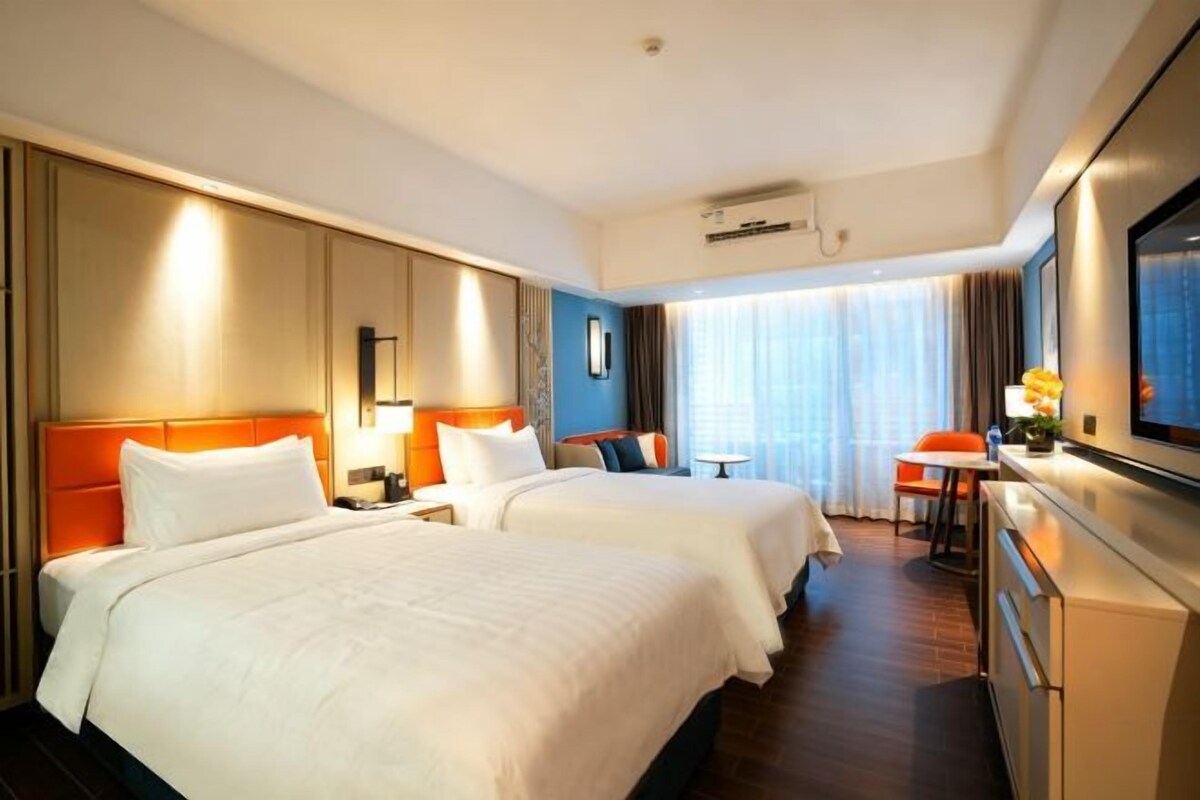 Quarto de hotel com duas camas, uma escrivaninha, televisão e janela com cortinas.
