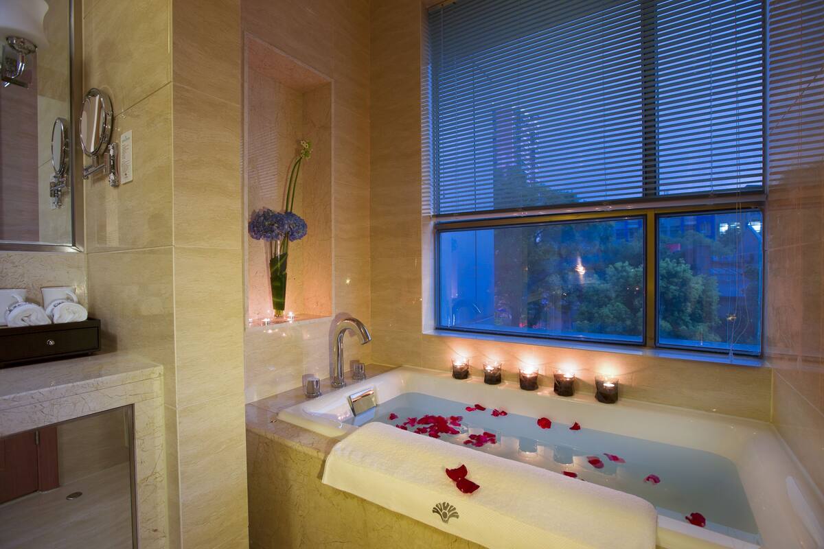 Ein Badezimmer mit einer Badewanne, einem Spiegel, einem Waschbecken und einem Fenster mit Jalousien.