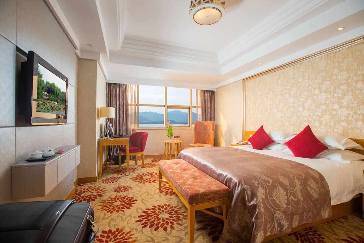 Ein Hotelzimmer mit einem großen Bett, einem Schreibtisch, einem Sessel, einem Fernseher und Blick auf die Berge.