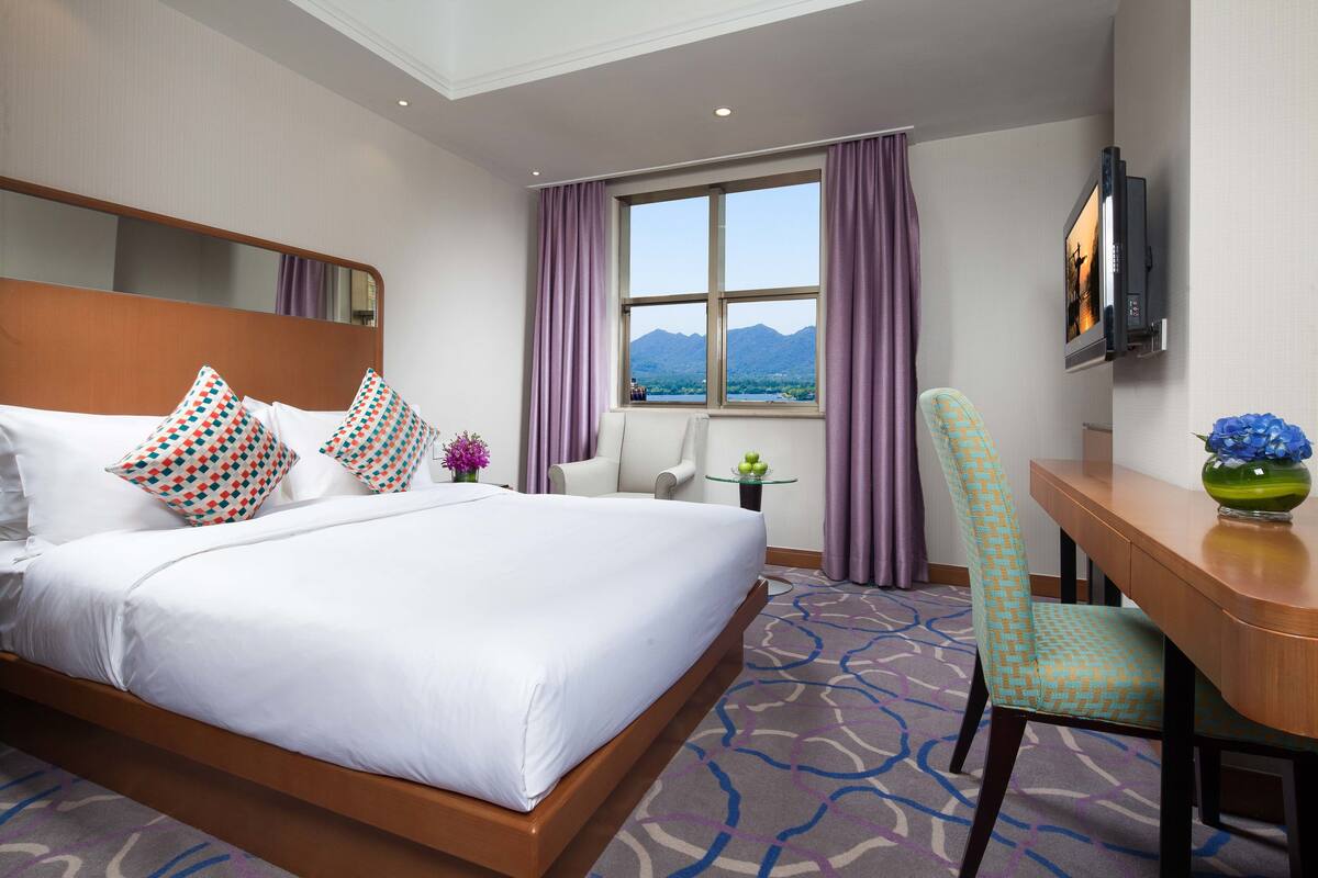 Ein Hotelzimmer mit einem großen Bett, einem Schreibtisch, einem Stuhl, einem Fernseher und einem Fenster mit Blick auf die Berge.
