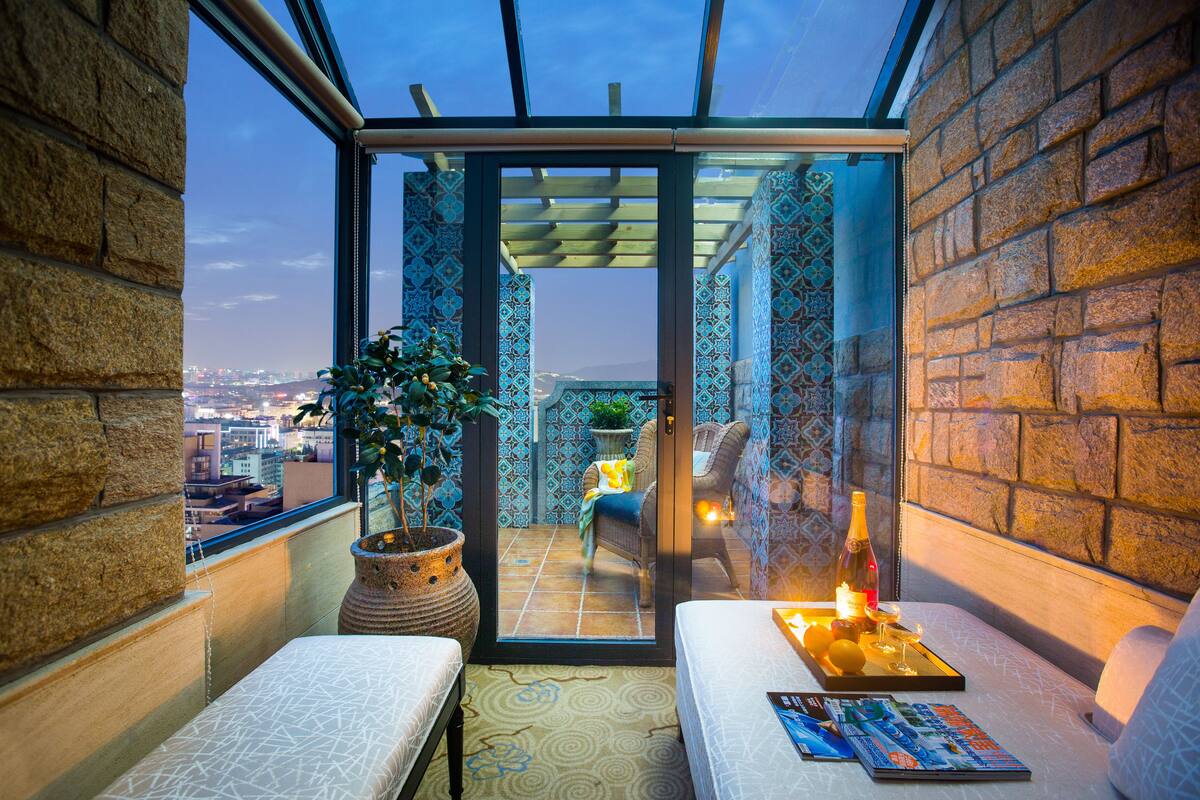 Ein Balkon mit Blick auf die Stadt, ein Sofa, ein Tisch mit Flasche und Gläsern sowie ein Blumentopf.